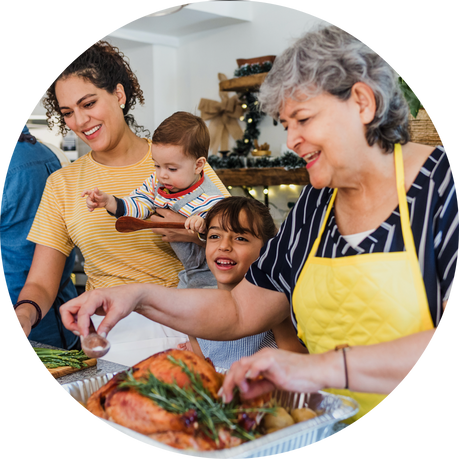 What we do Group photo: Older woman wearing yellow apron with two grandchildren and daughter cooking food.